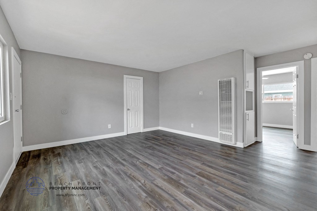 an empty living room with wood flooring and a door to the kitchen