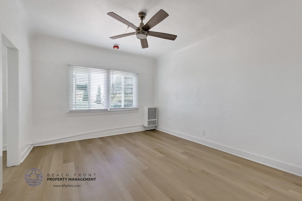 a bedroom with white walls and wood floors and a ceiling fan
