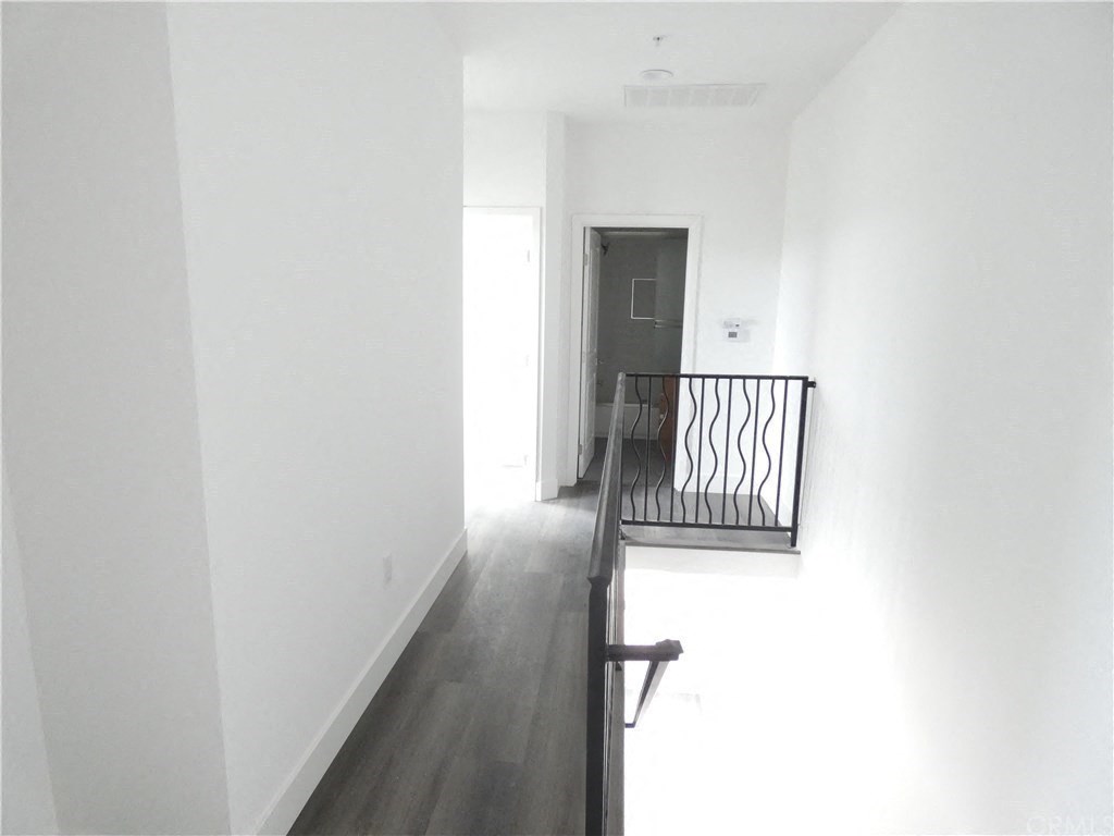an empty hallway with white walls and a black railing and a door
