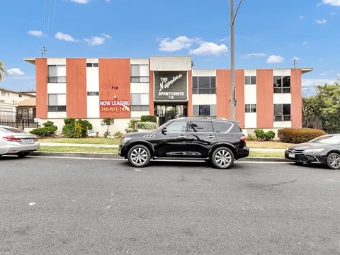 A black SUV is parked in front of a building with a sign that says "Now Leasing.".
