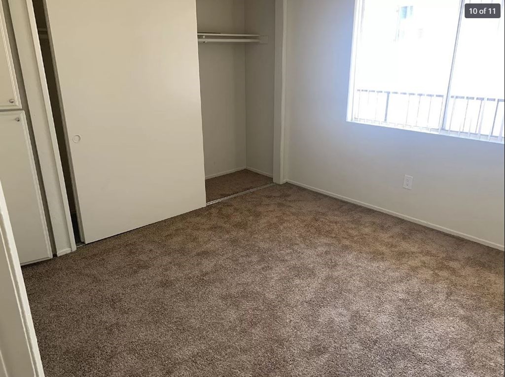 A room with carpeted floor and a window with blinds.