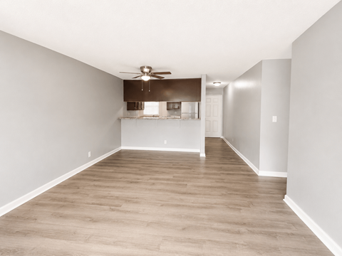 A spacious room with a ceiling fan and a kitchenette in the background.