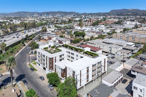 A modern building with a green roof is surrounded by other buildings and a busy street.