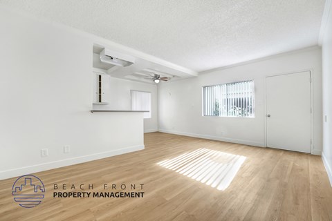 A spacious room with wooden floors and white walls, with a window covered by blinds.