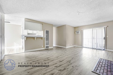 A spacious room with wooden flooring and a logo for Beach Front Property Management in the corner.
