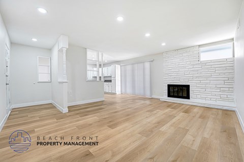 A spacious room with wooden flooring and a fireplace.