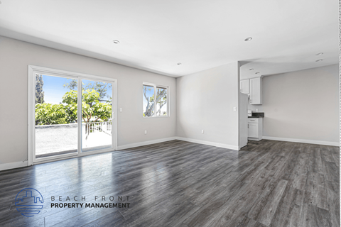 A spacious room with wooden flooring and a view of the beach through the sliding glass doors.