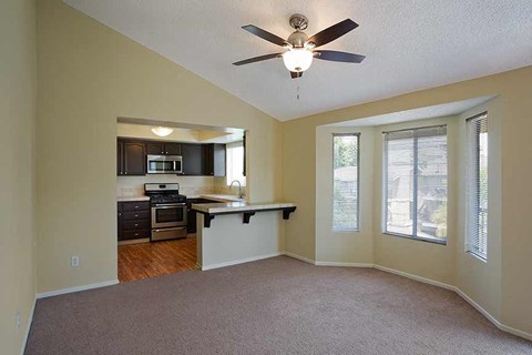 an empty living room with a kitchen and a ceiling fan