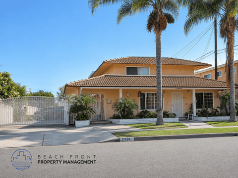 A house with a fence and palm trees in front of it.