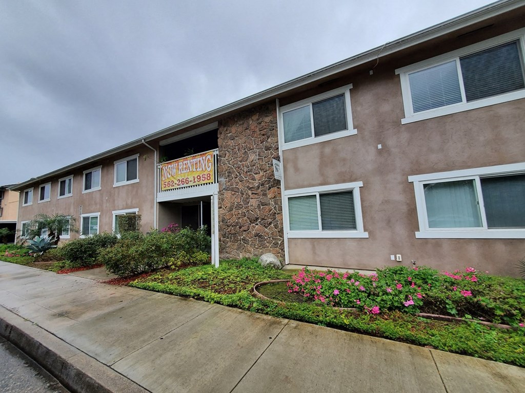 an apartment building with a sidewalk and landscaping in front of it