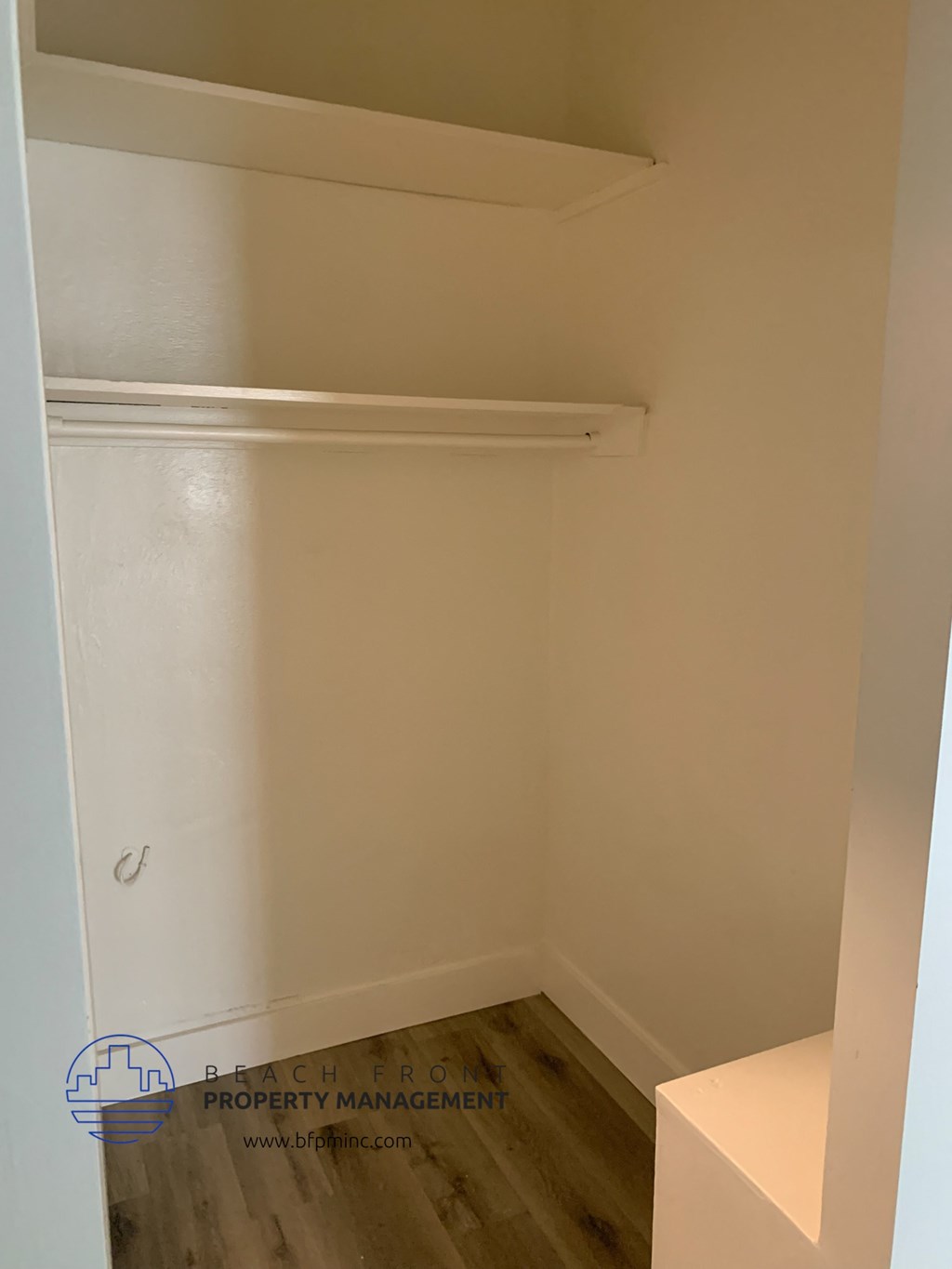 a walk in closet with a white shelf and a wood floor