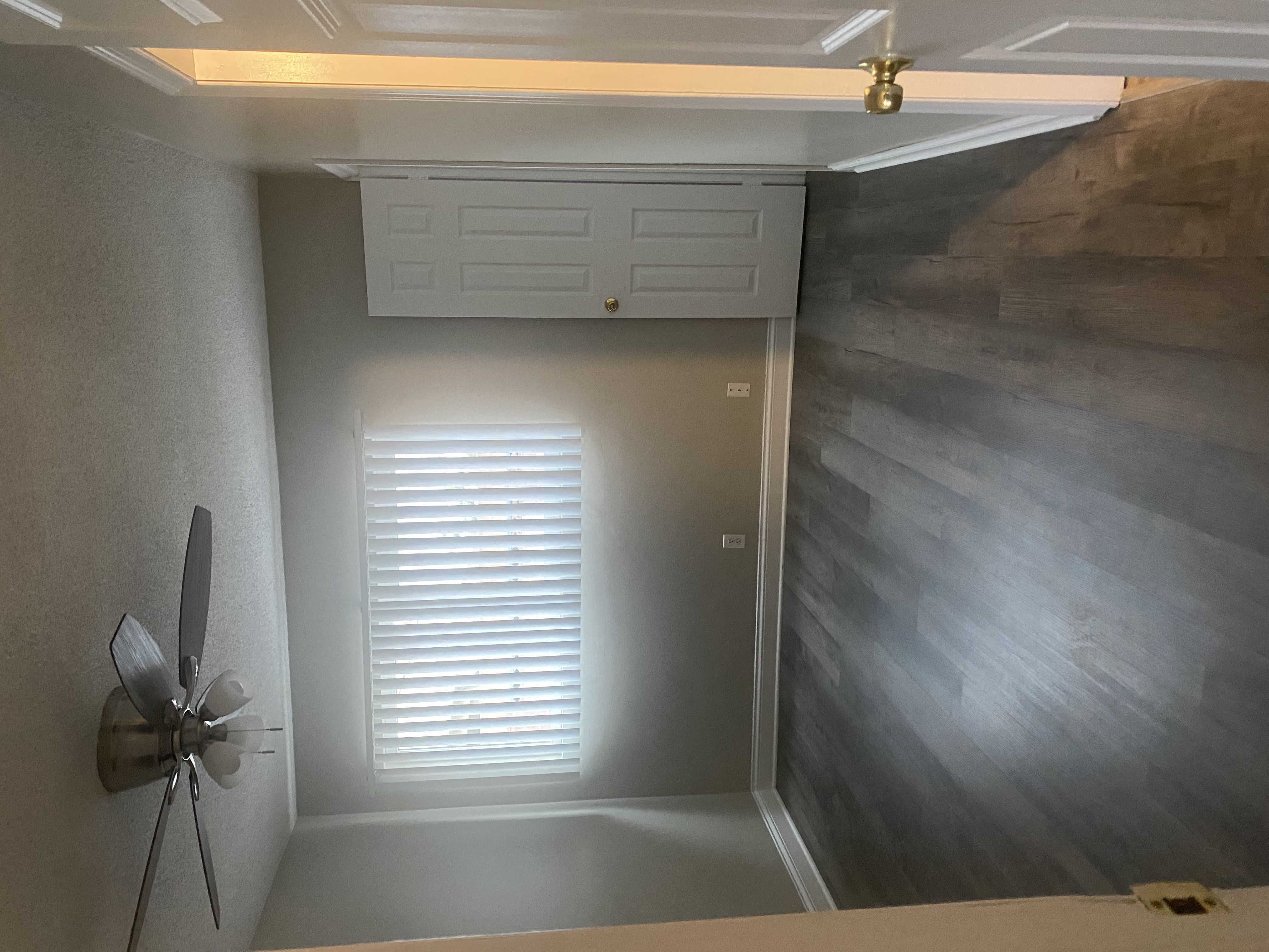 a room with a vaulted ceiling and a window with white shutters