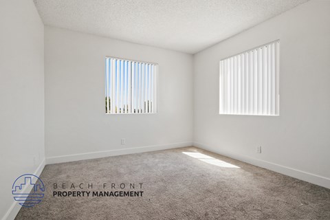 A room with a carpeted floor and two windows with blinds.