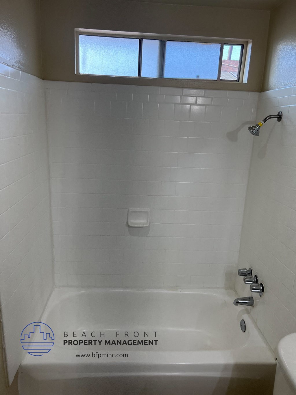 a white tiled bathroom with a tub and a window