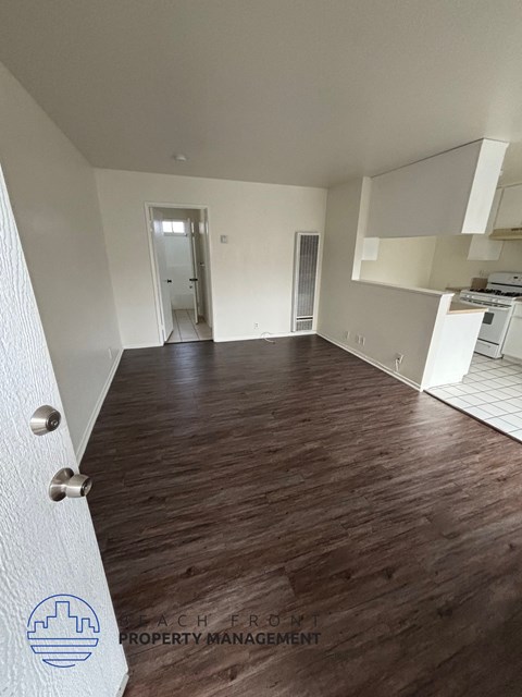 A room with wooden flooring and white walls, with a logo for Beach Front Property Management in the bottom left corner.