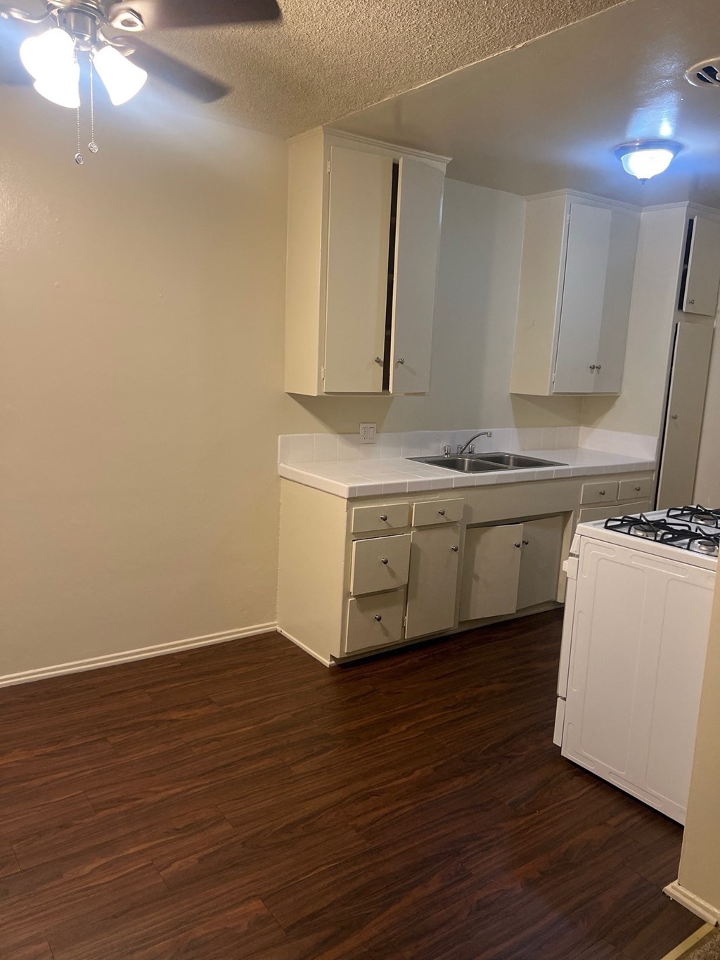 an empty kitchen with wood flooring and white cabinets and appliances