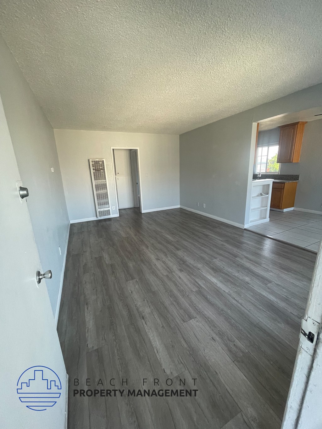 an empty living room with wood flooring and a kitchen