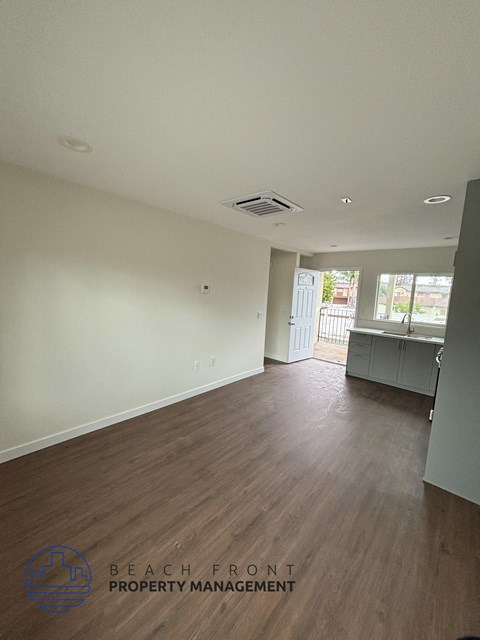 A spacious room with wooden flooring and a white wall.