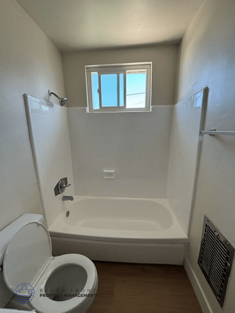 A white bathroom with a toilet, tub, and window.