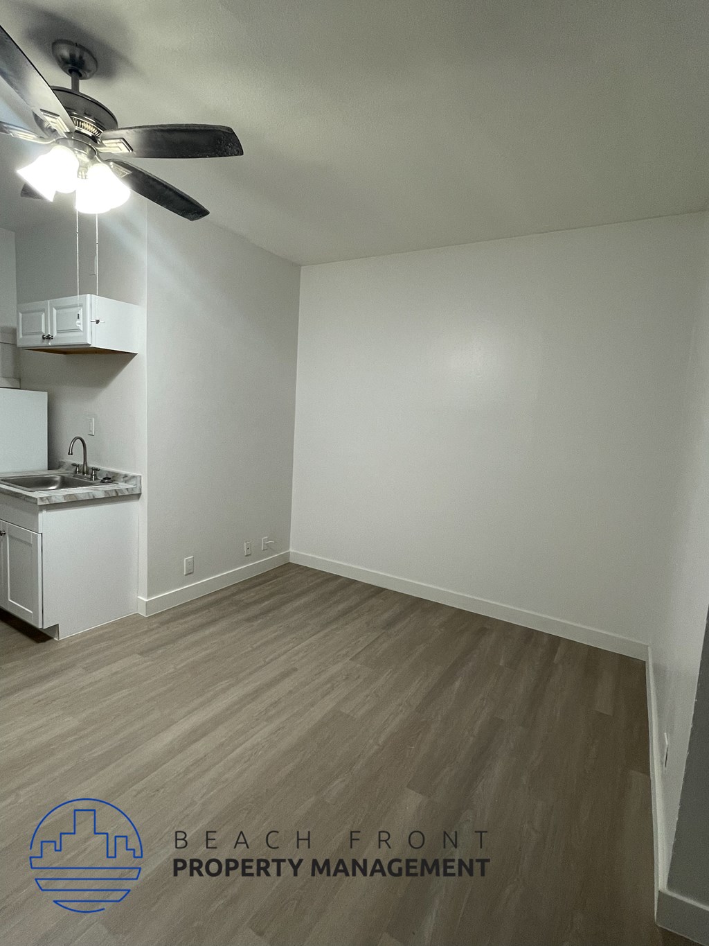 an empty room with a kitchen and a ceiling fan