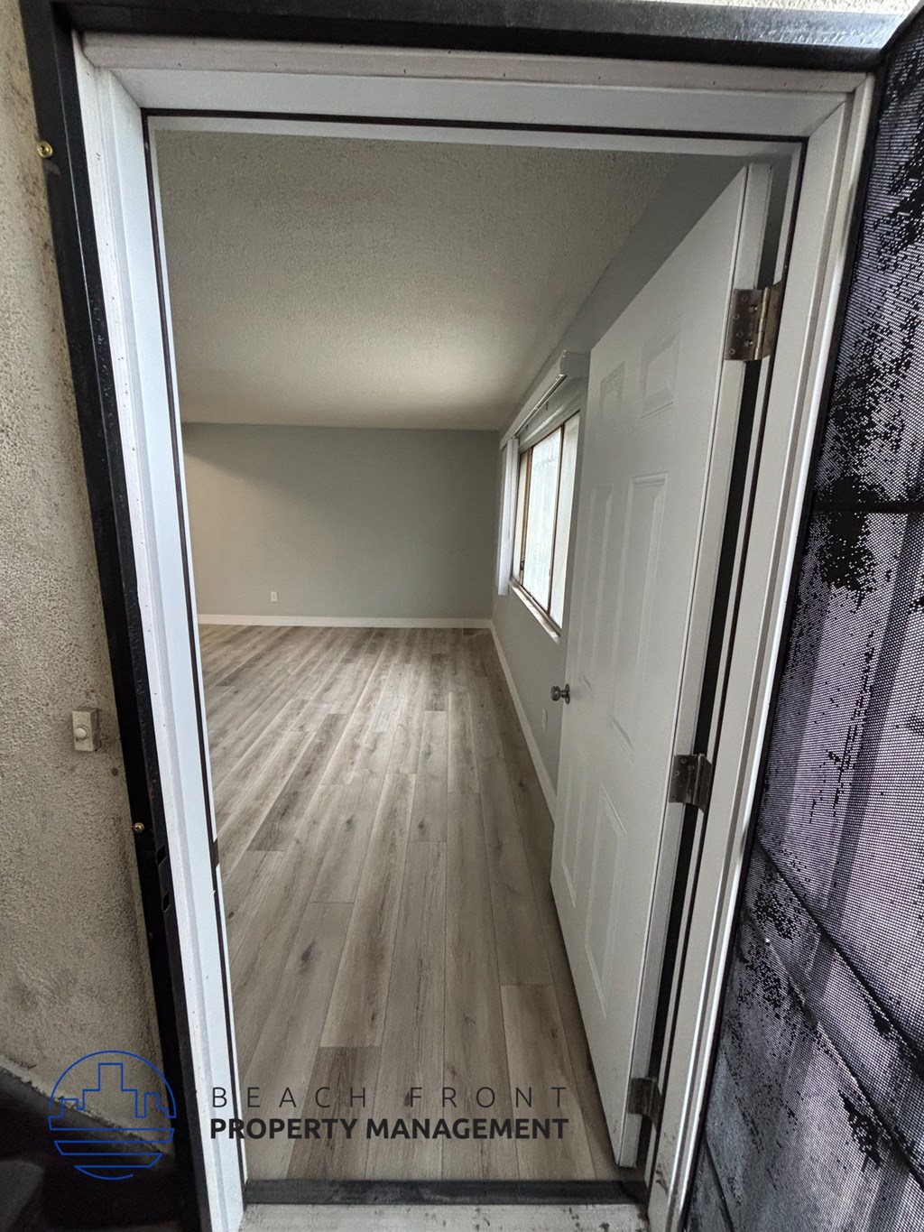 A doorway opens to a hallway with wooden floors and white walls.
