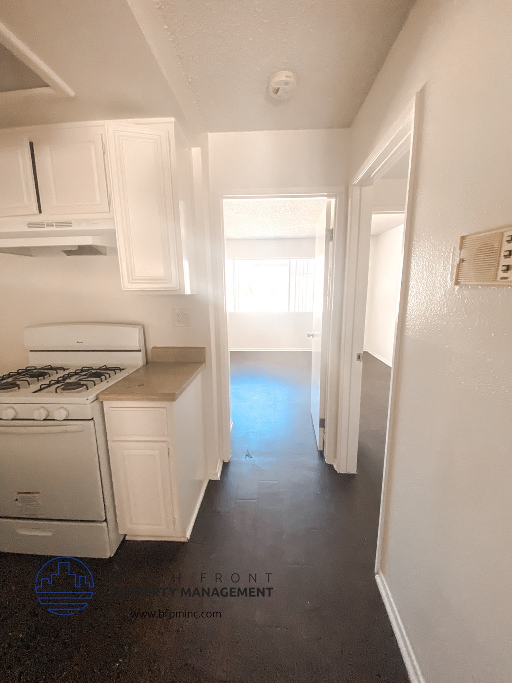 an empty kitchen with white cabinets and a stove and a window