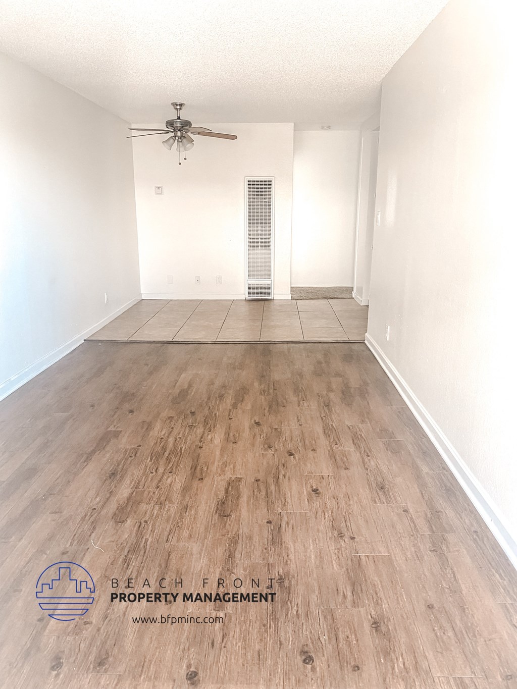the spacious living room with hardwood flooring and a ceiling fan