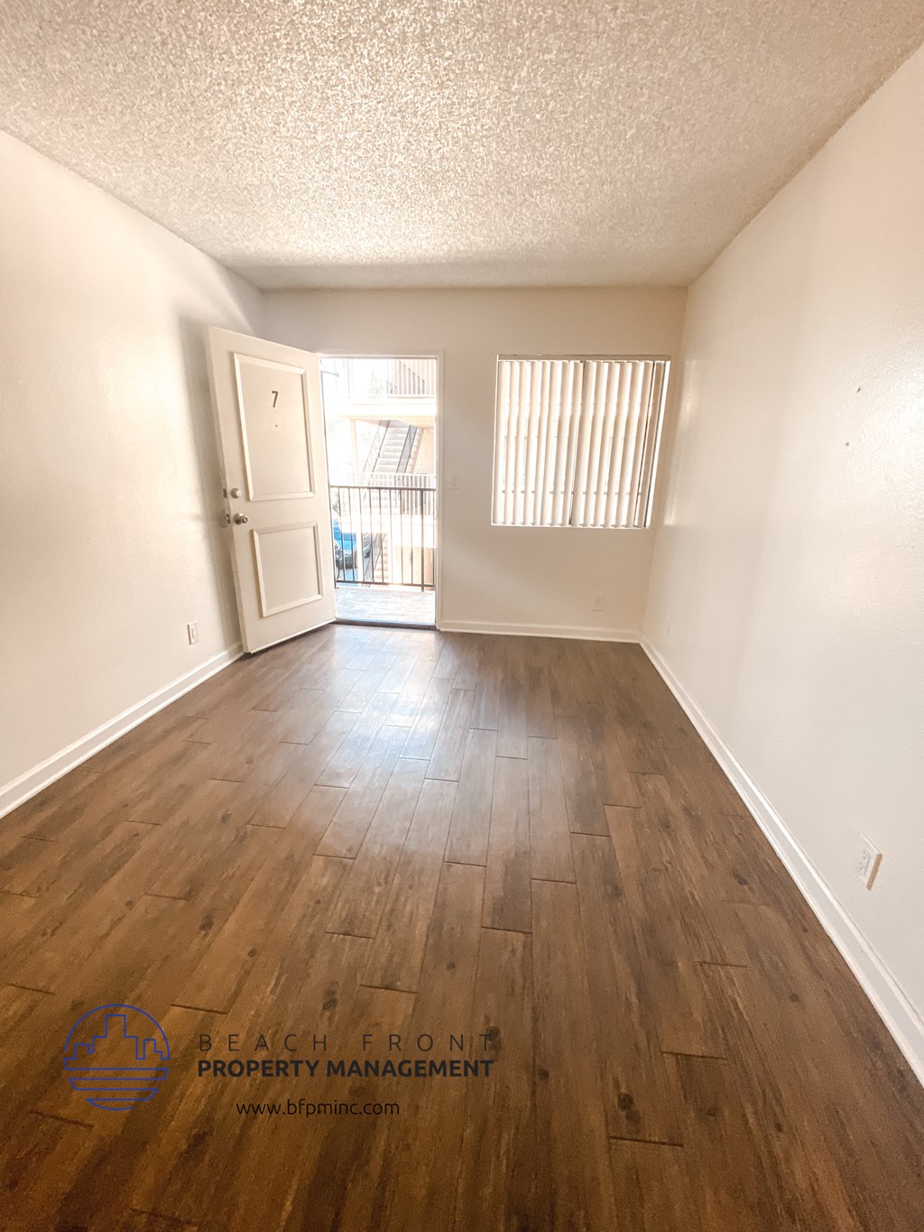 an empty living room with wood flooring and a door to a balcony