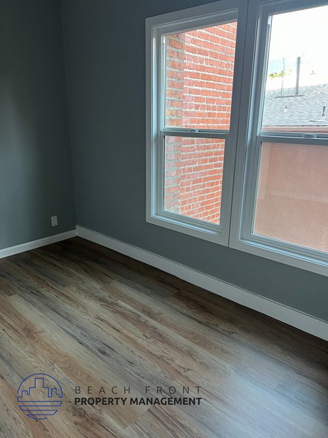 A room with a wooden floor and a window showing a brick wall outside.