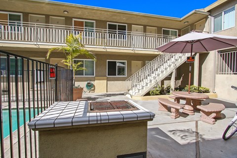 A poolside table with a tiled top is in the foreground of a sunny courtyard.