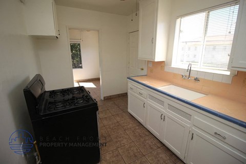A kitchen with white cabinets and a black trash can.
