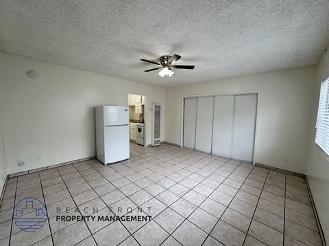 A spacious room with a ceiling fan and a refrigerator.