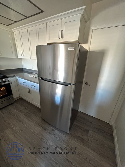 A stainless steel refrigerator in a kitchen with wooden flooring.
