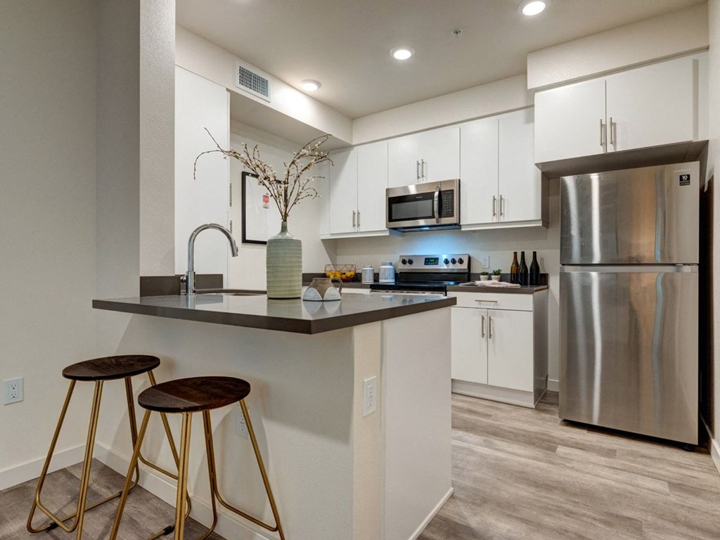 a kitchen with a island with two stools and a stainless steel refrigerator