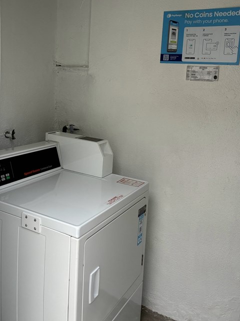 A white washing machine sits next to a wall with a sign that says "No Coins Needed".