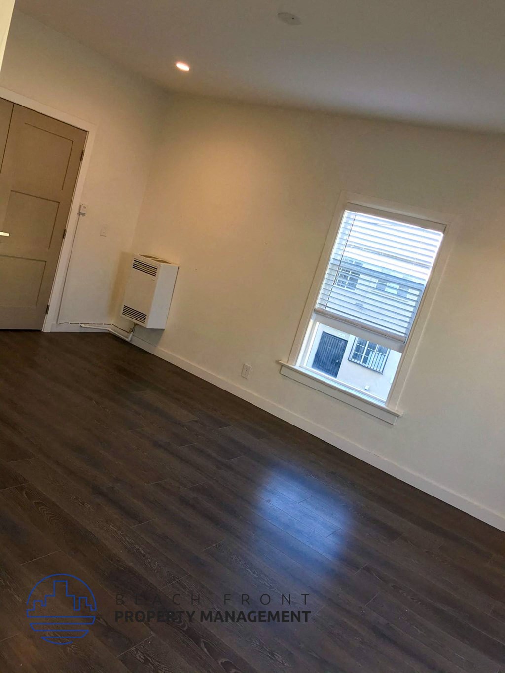 the living room of a home with a window and wooden floors