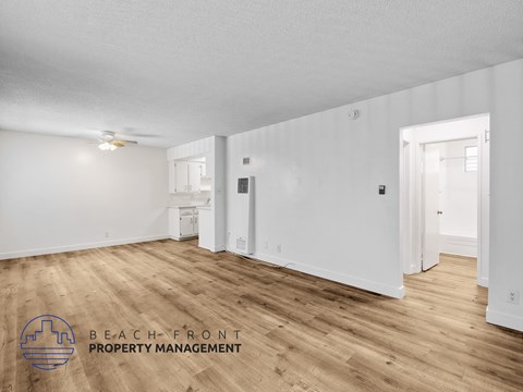 A spacious room with wooden flooring and white walls, with a logo for Beach Front Property Management in the bottom left corner.