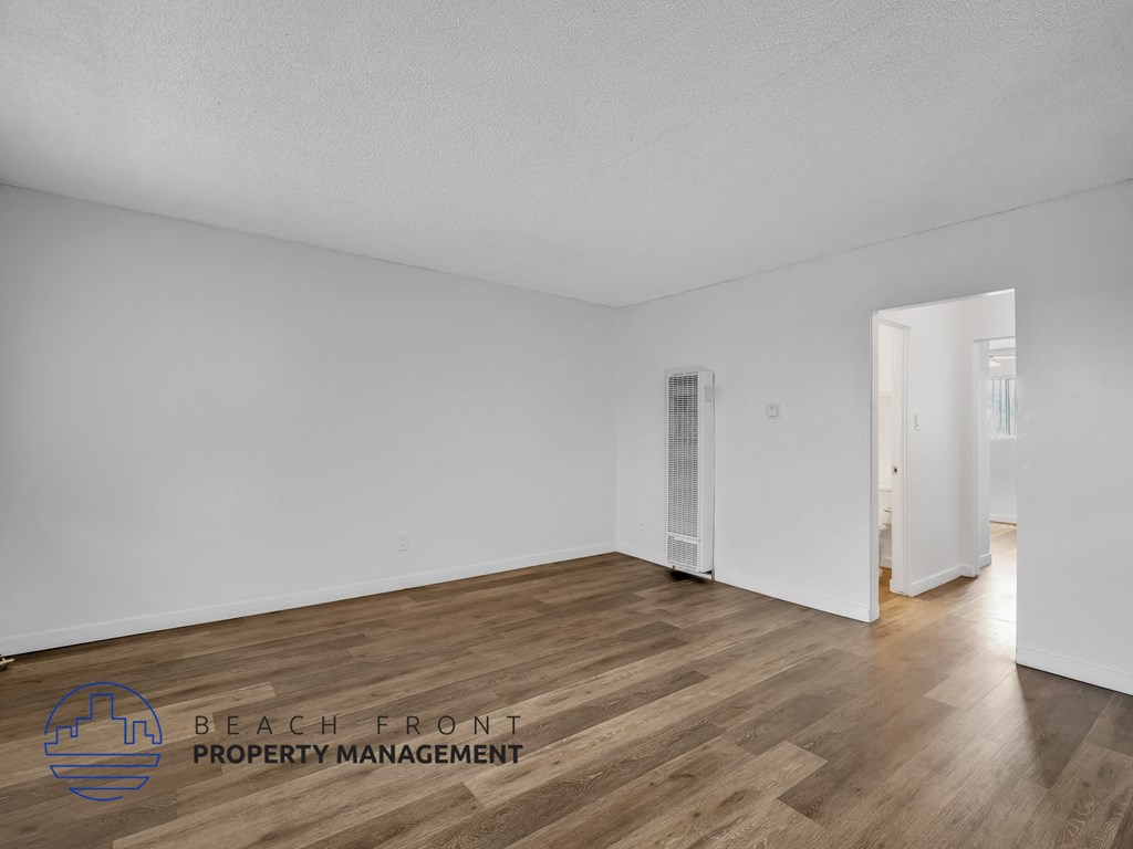 A spacious room with wooden flooring and white walls, with a doorway leading to another room.