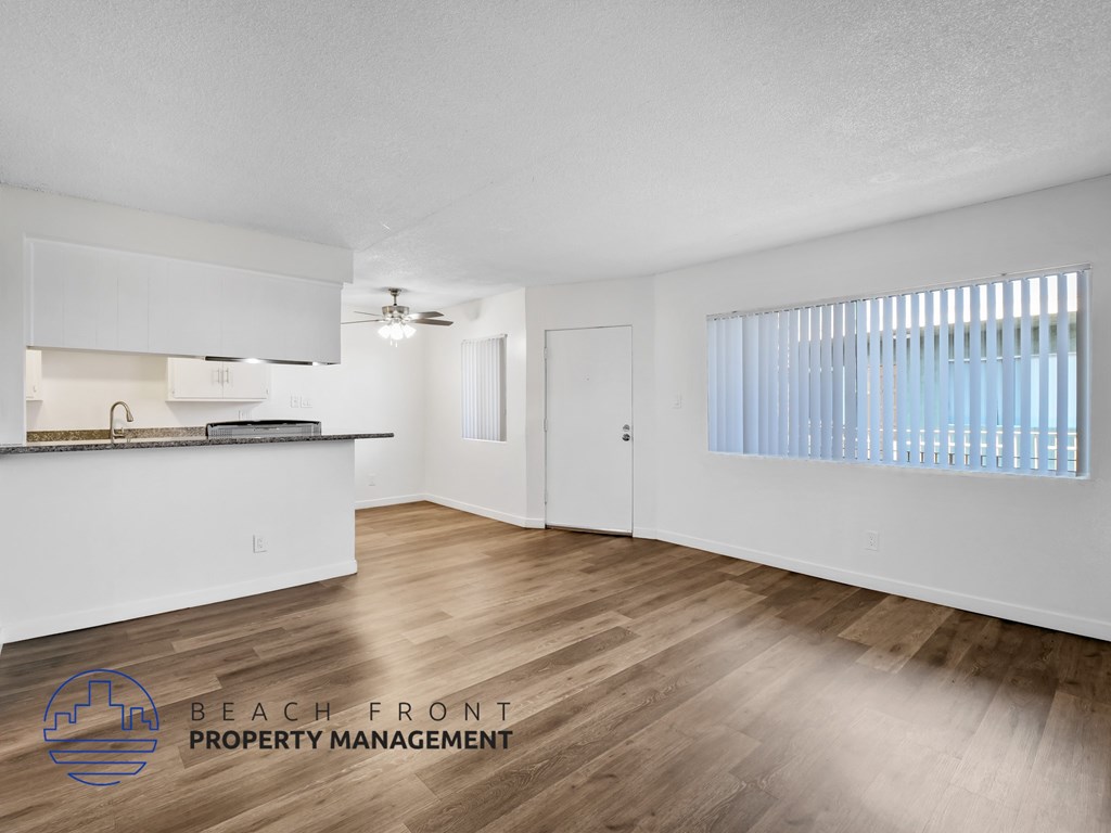 A spacious room with wooden flooring and a window with blinds.