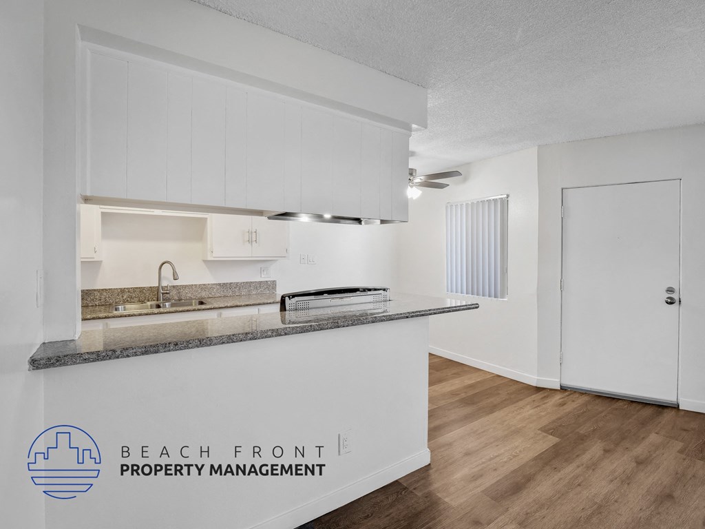 A kitchen with white cabinets and a countertop with a logo for Beach Front Property Management.