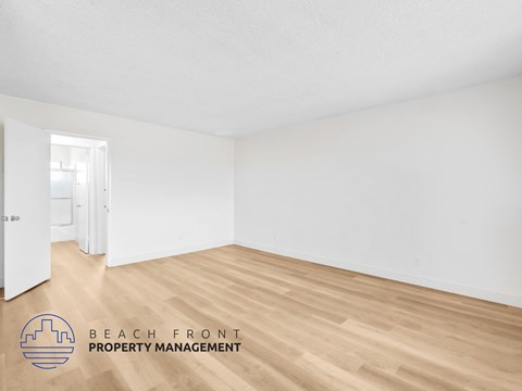 A room with wooden flooring and white walls, with a doorway leading to another room.