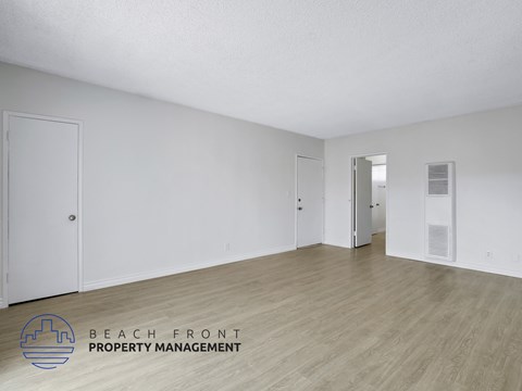 A room with wooden flooring and white walls, with a door on the left and another door on the right.