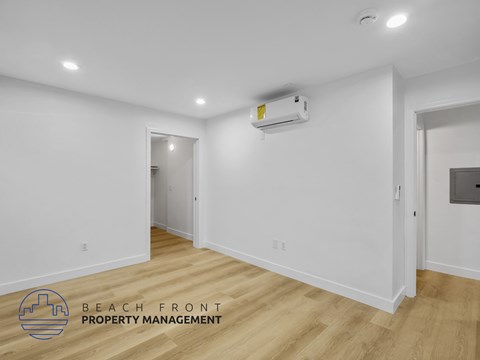 A spacious room with wooden flooring and a white wall with a window.