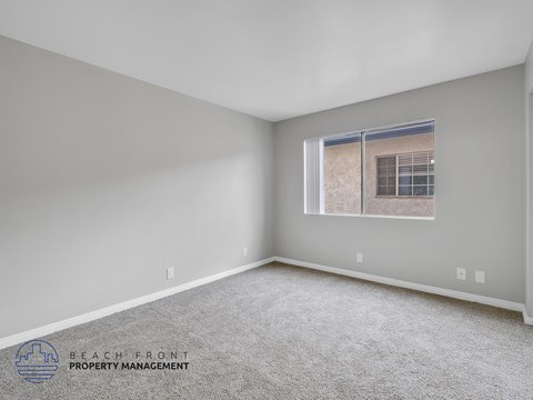 A spacious room with a carpeted floor and a window showing a building outside.