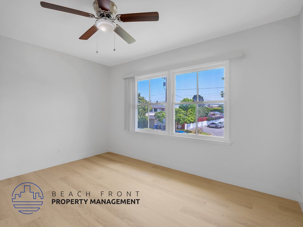 A room with a ceiling fan and a window showing a view of a street and buildings.