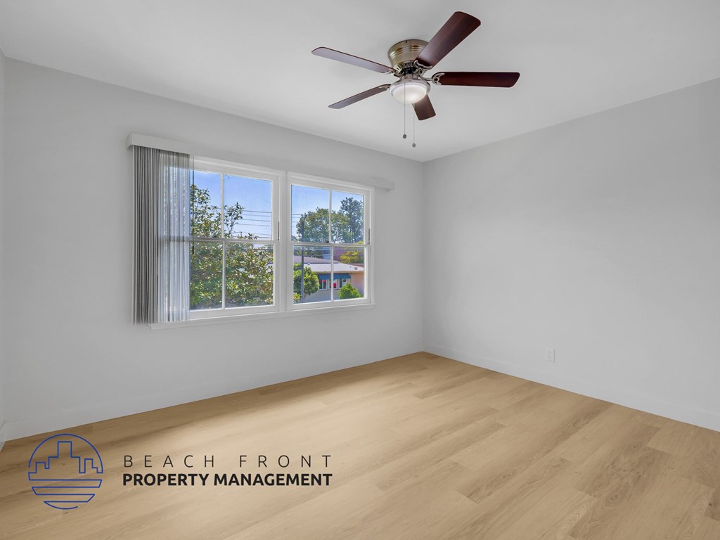 A room with a ceiling fan and a window overlooking a residential area.