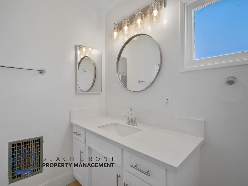 A bathroom with a white countertop and two round mirrors.