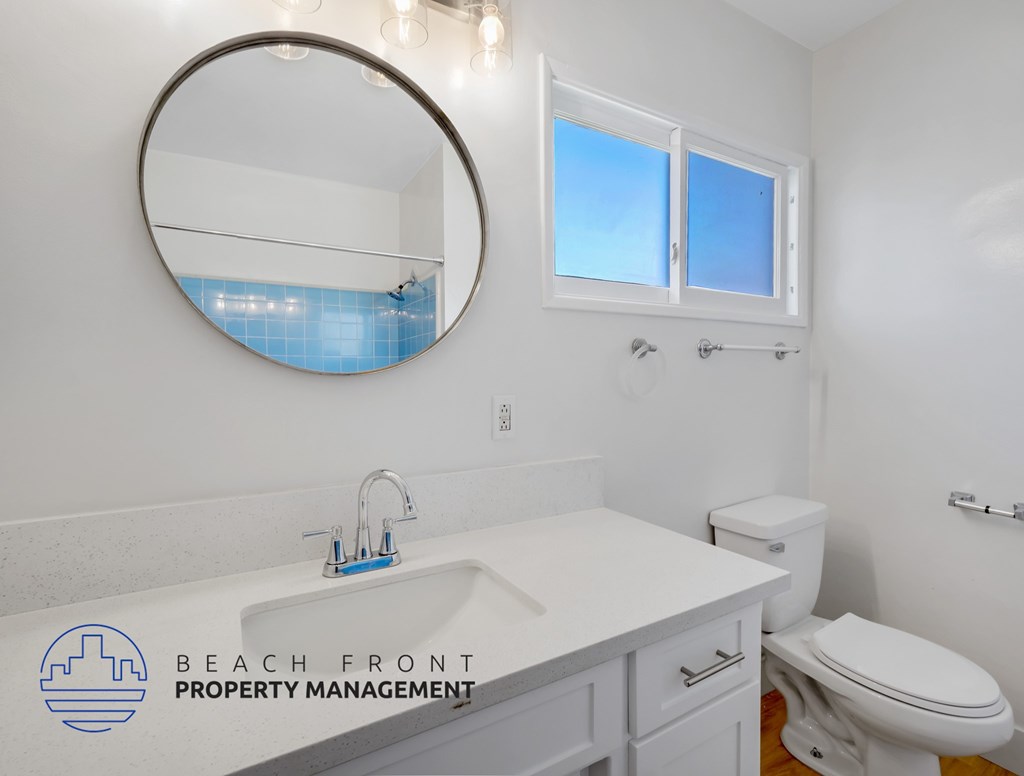 A bathroom with a white counter top and a round mirror.