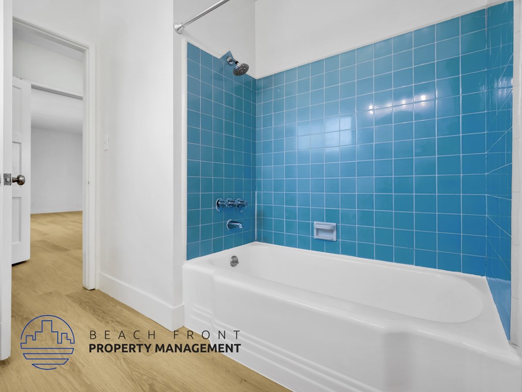 A white bathtub with blue tiles on the wall.