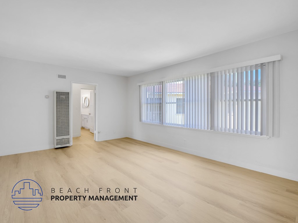 A spacious room with wooden flooring and a window with blinds.